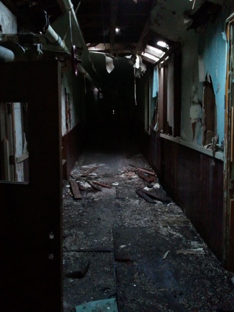 Dark, abandoned hallway inside a Brigham City Indian School building, with a collapsed ceiling, peeling paint, and debris, taken before demolition in Dec 2012.