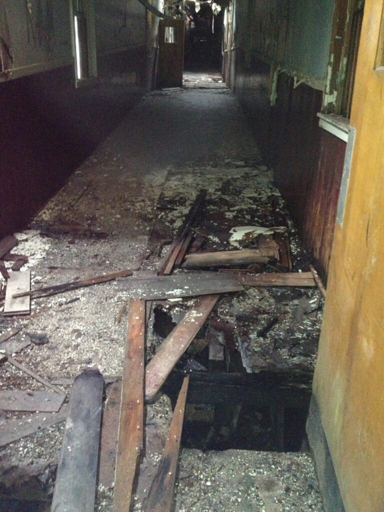 Decayed hallway with a large hold in the floor at Brigham City Indian School