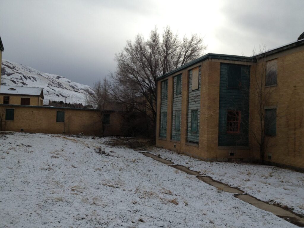 Abandoned Brigham City Indian School in winter, with boarded windows and peeling paint.