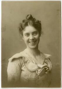 Portrait of Maud May Babcock, a pioneering drama educator, wearing a lace-trimmed dress with a bow, smiling warmly at the camera.